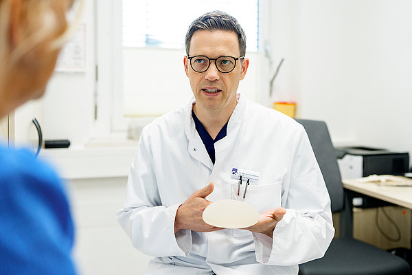 Arzt hat ein Implantat in der Hand und erklärt Patientin das Vorgehen
