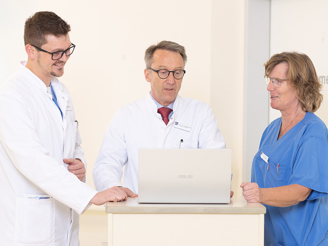 Gespräch zwischen Ärzten und einer Pflegekraft an einem Laptop
